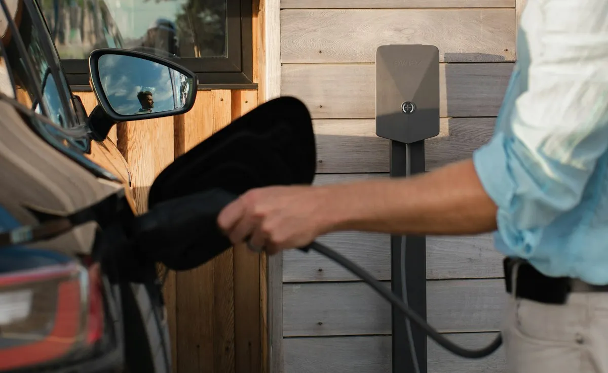 Muž zapojuje do auta nabíjecí kabel z wallboxu na zdi domu